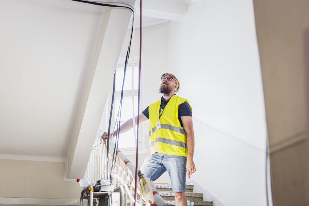 Tekninen isännöitsijä liivissä ja kypärässä rappukäytävässä